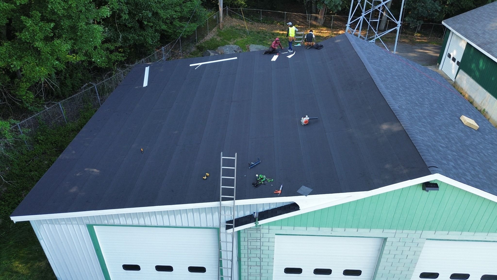 A Superior Roofing crew on a garage roof with a ladder, rolling out new asphalt roofing