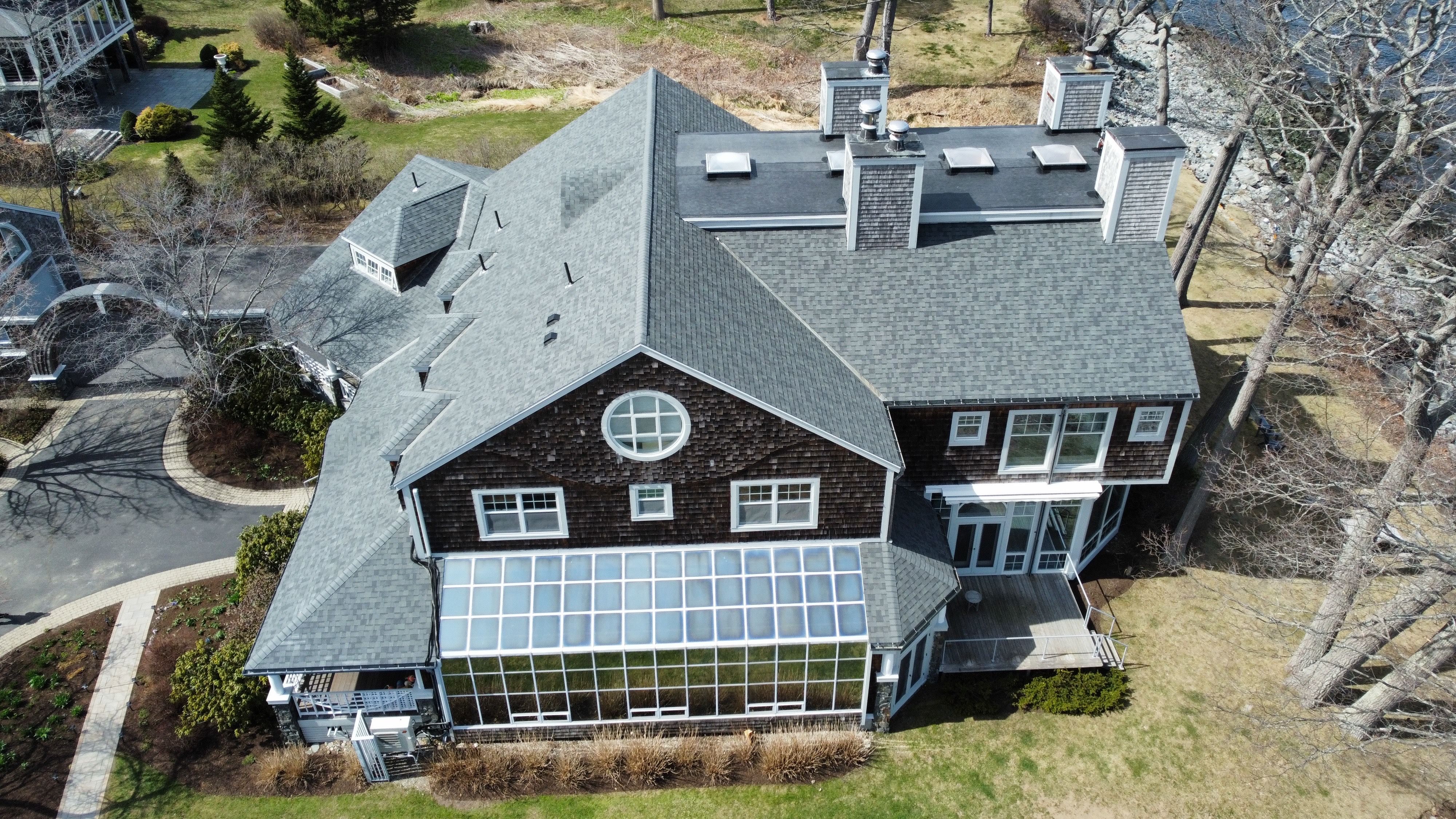 A new grey shingle roof Superior Roofing put on a shingle-style house by the water, seen from a drone