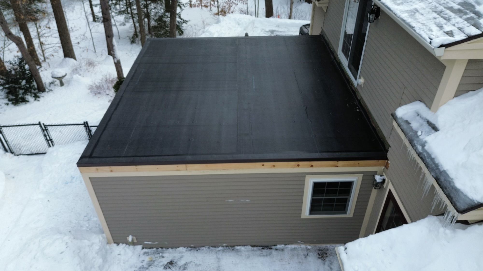 A black rubber flat roof on an addition, finished, with snow on the ground