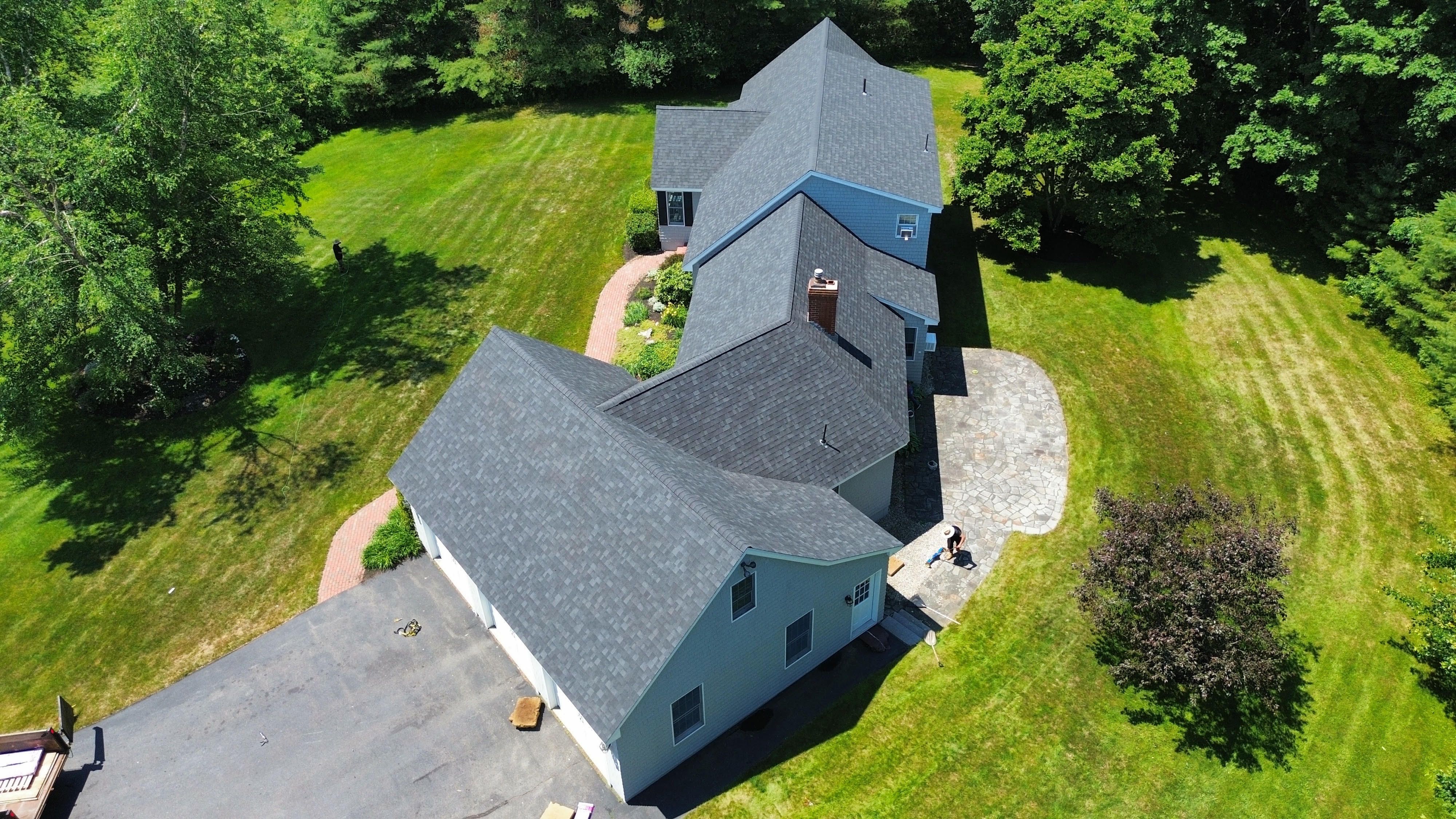 A new shingle roof on a gray house in the woods, seen from a drone