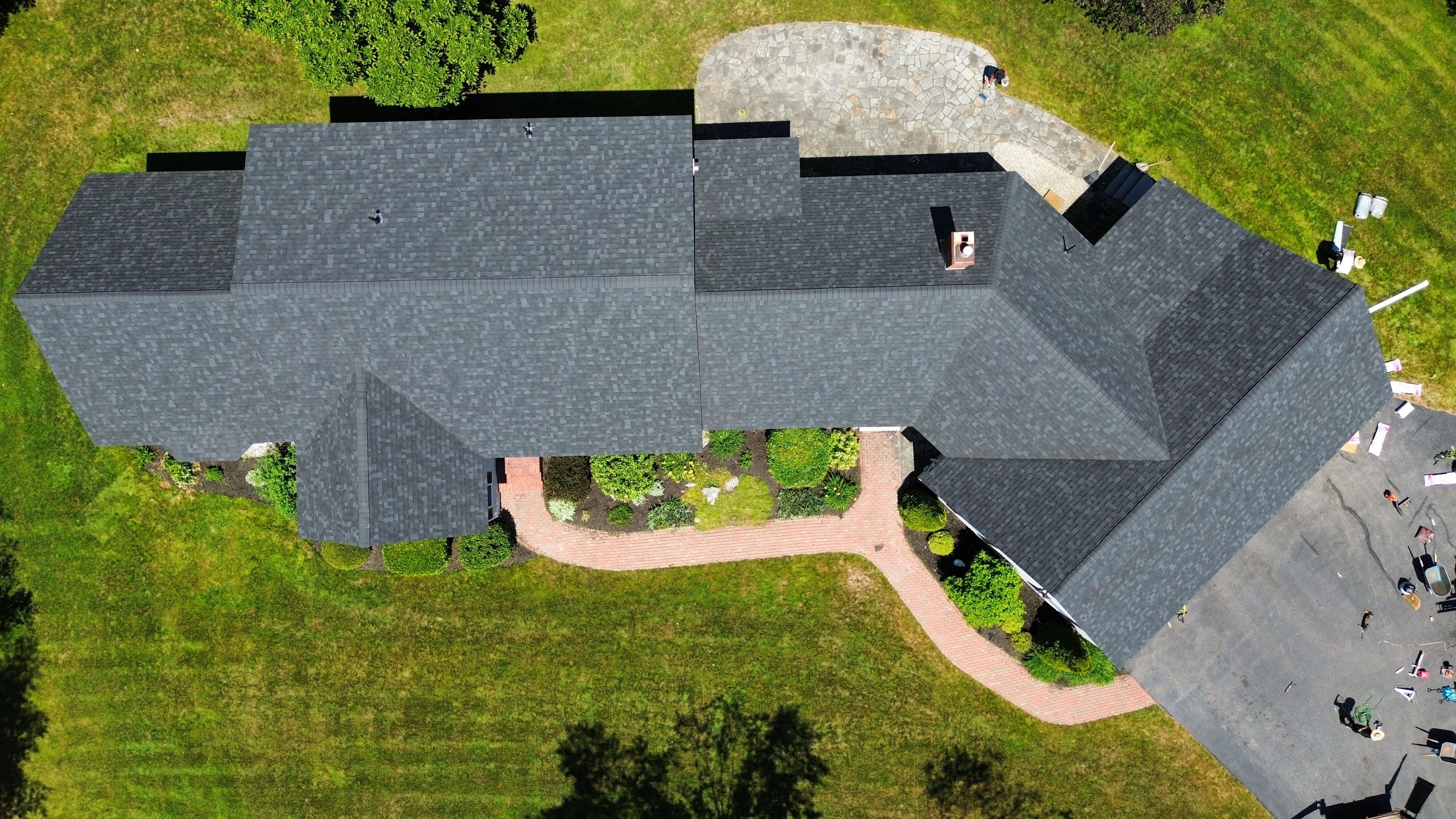 A new gray shingle roof on a long ranch house with a brick path, seen from above