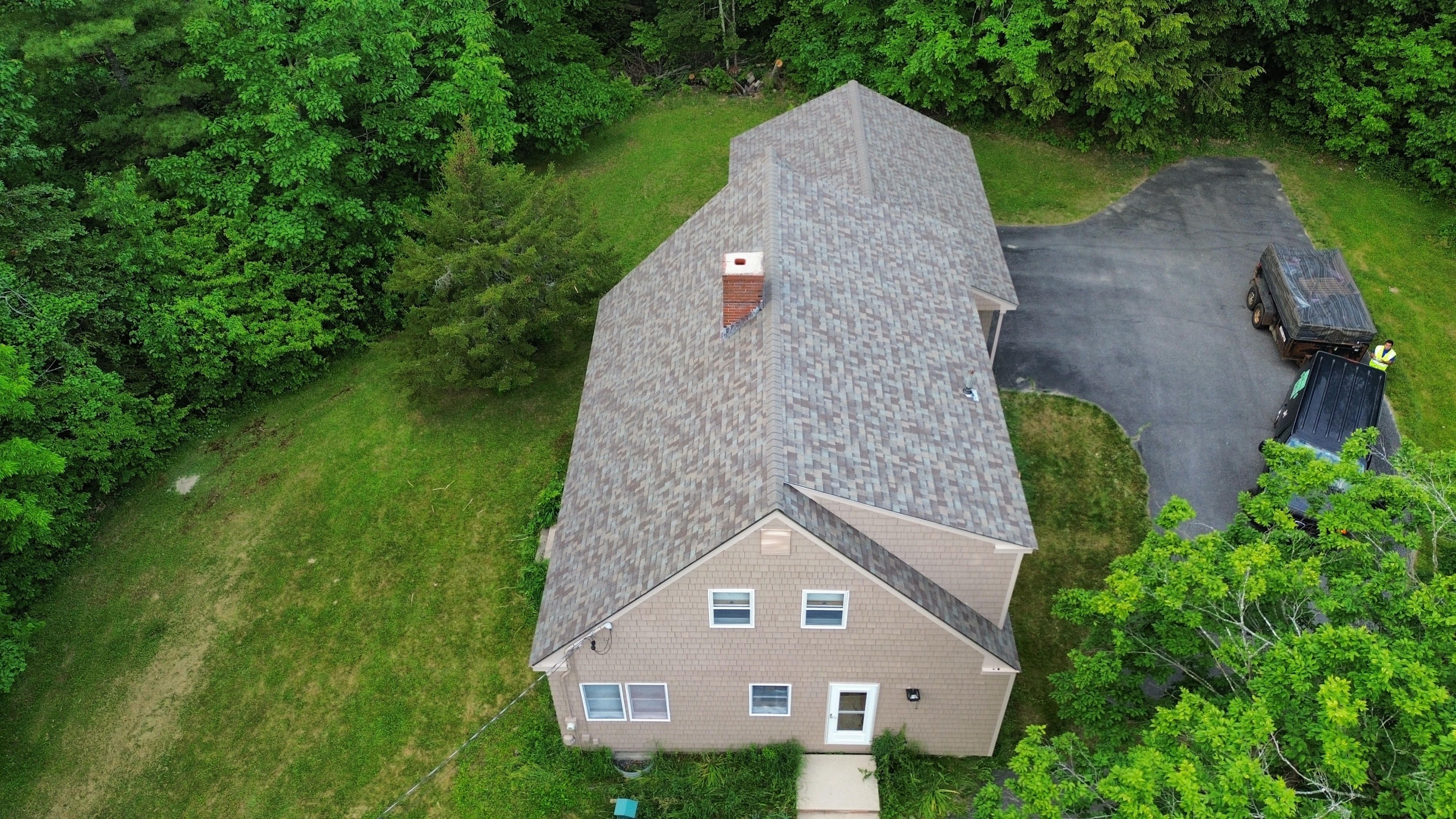 A new shingle roof on a tan saltbox in the trees, seen from a drone