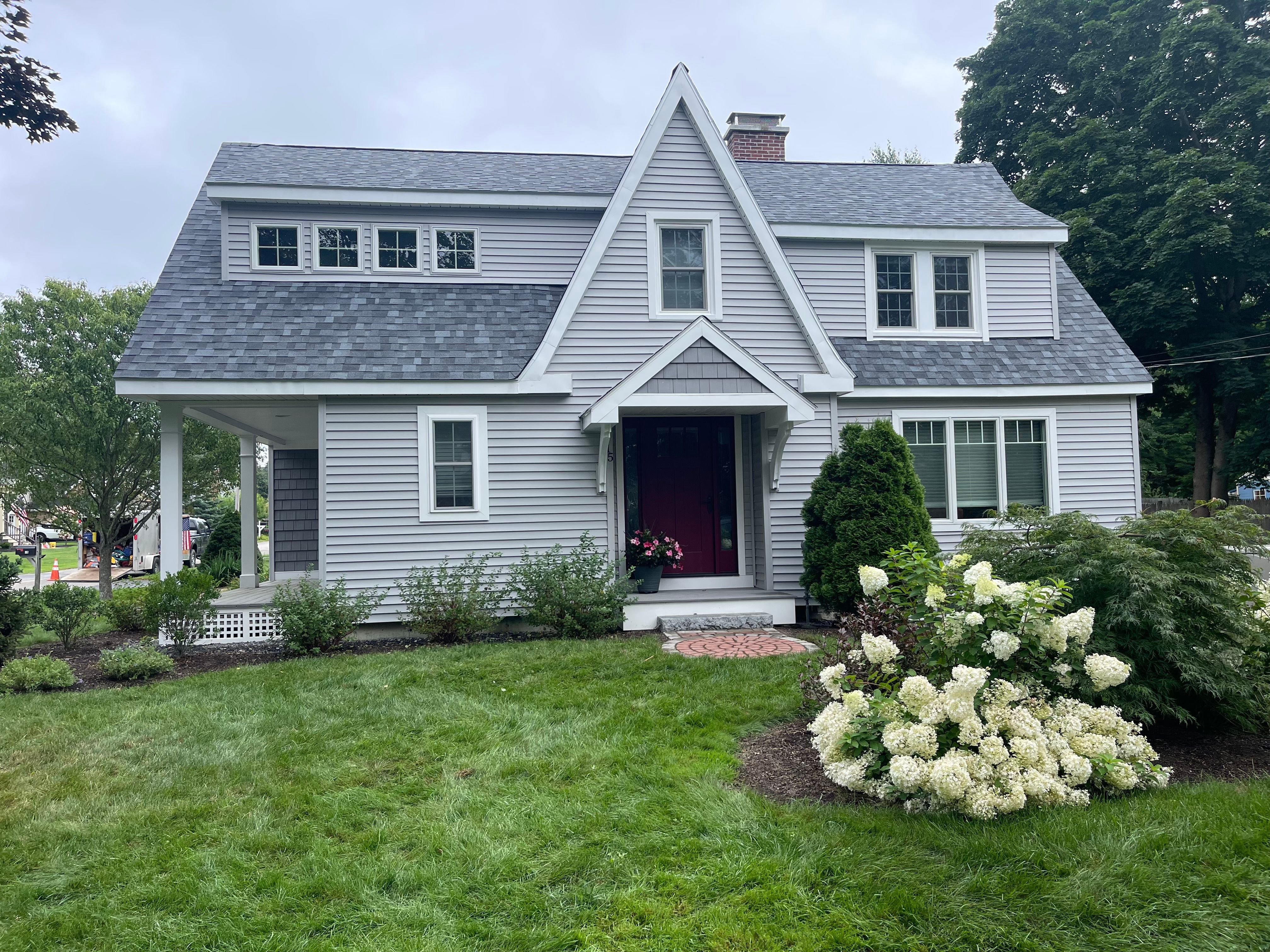 A finished gray shingle roof on a cape with white hydrangeas in front
