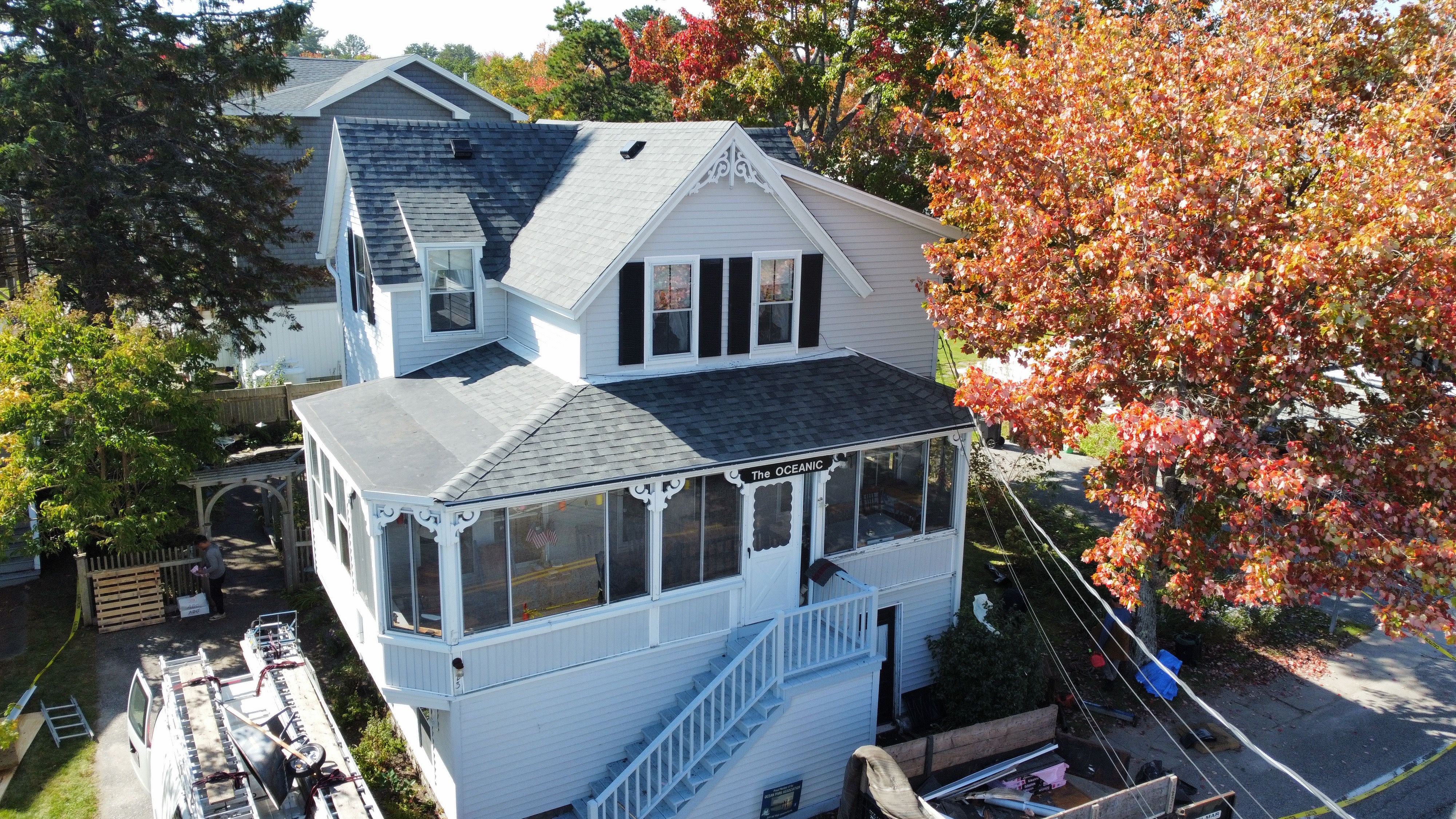 A new gray shingle roof on a cottage with a screened porch and fall color