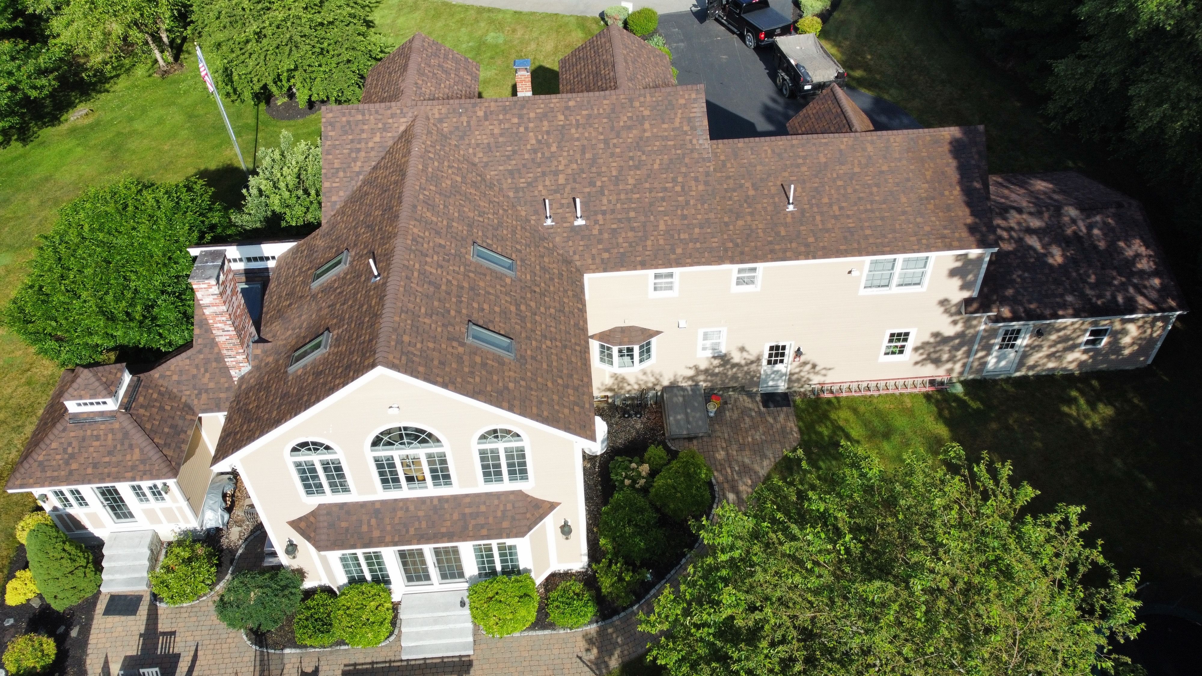 A new brown shingle roof on a large colonial home, seen from a drone