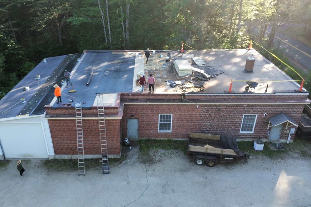 A Superior Roofing crew laying a white rubber membrane on a flat commercial roof