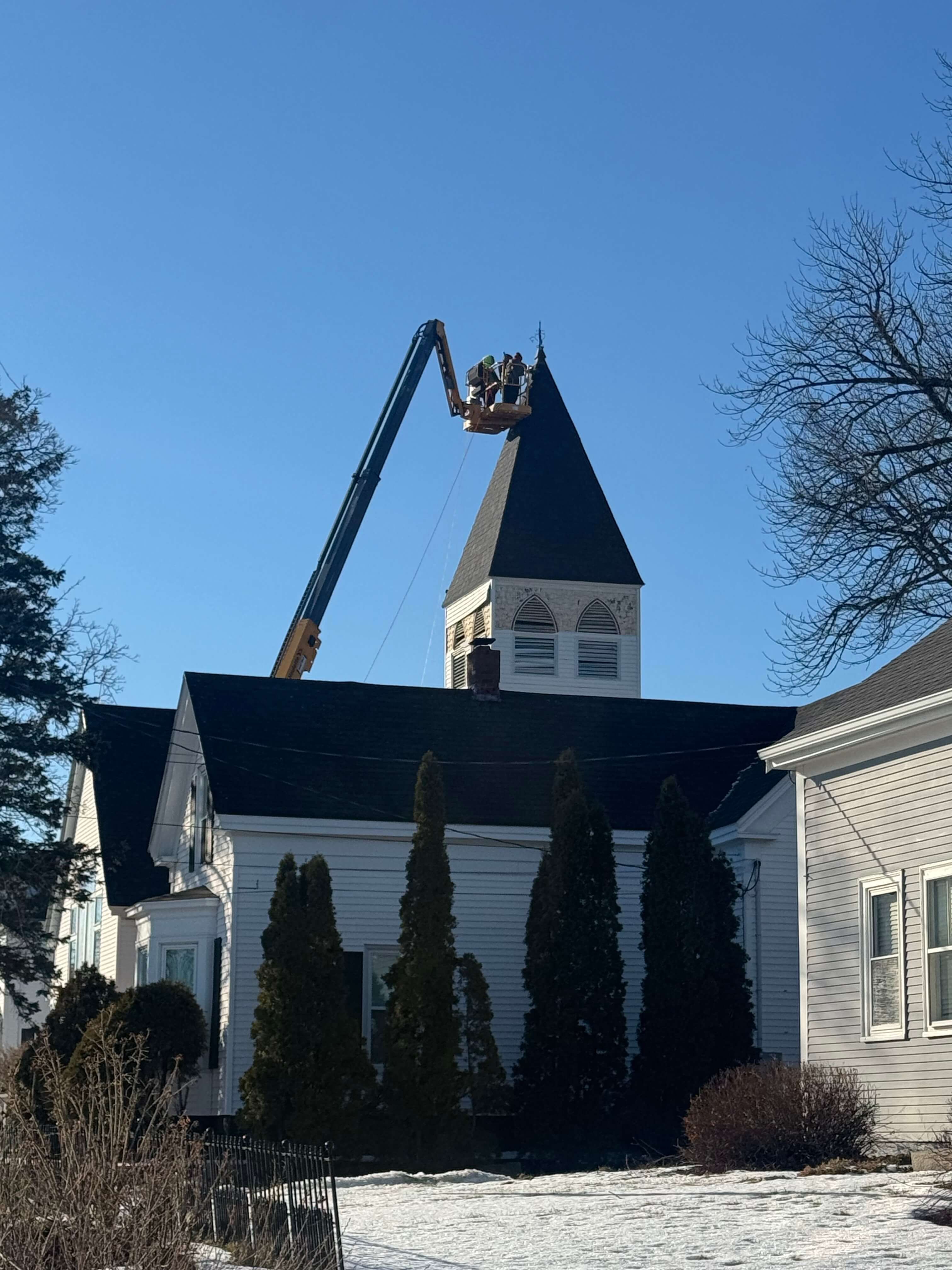 A Superior Roofing crew working from a lift high on a commercial building with a steeple